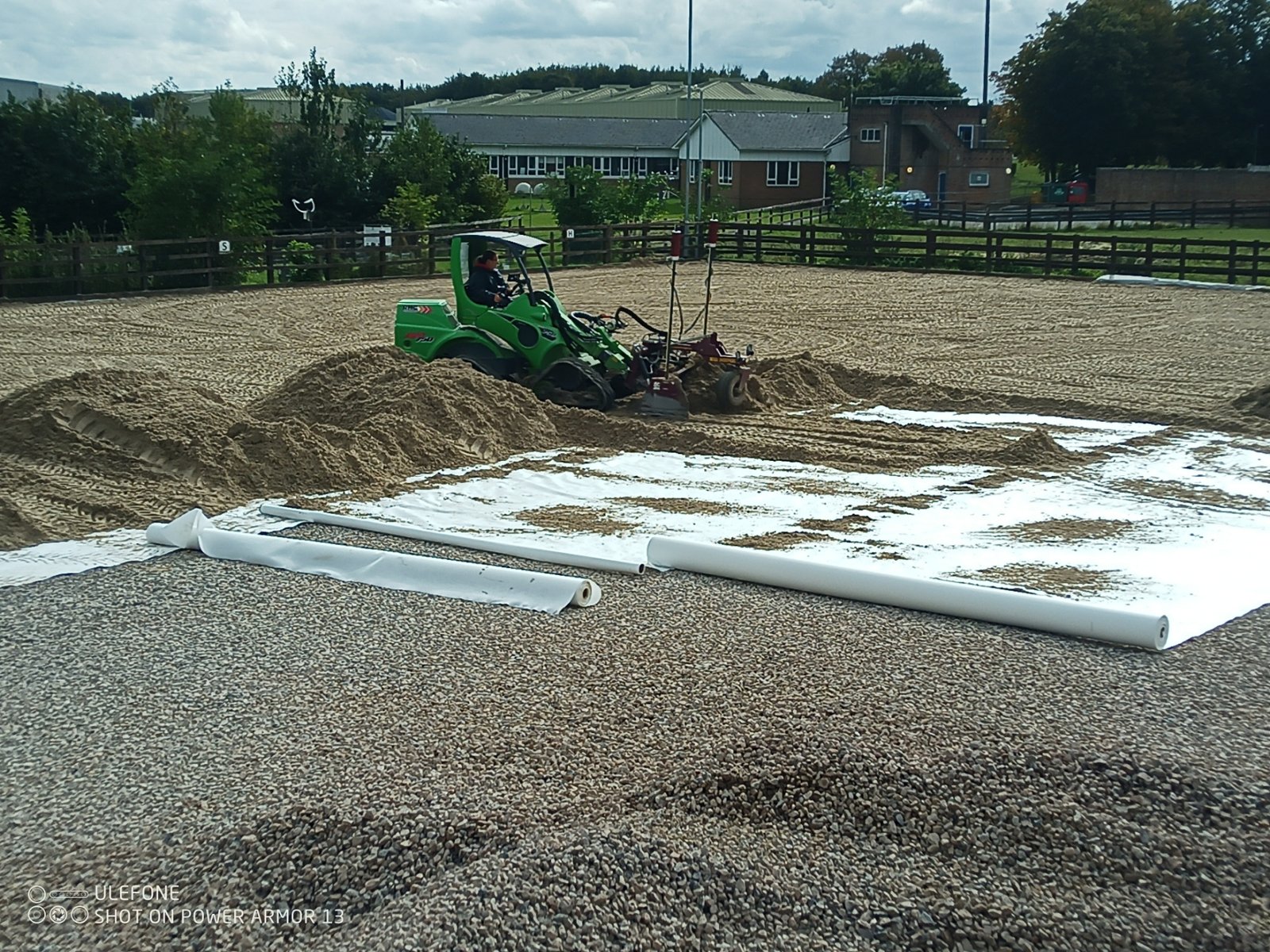 Grading silica sand over a 200 gsm non-woven geotextile membrane, with 20–40 mm carboniferous limestone base visible beneath the edge, using an Avant loader and SharpGrade box grader at the Royal Artillery Saddle Club, Larkhill — AG Rural Solutions.